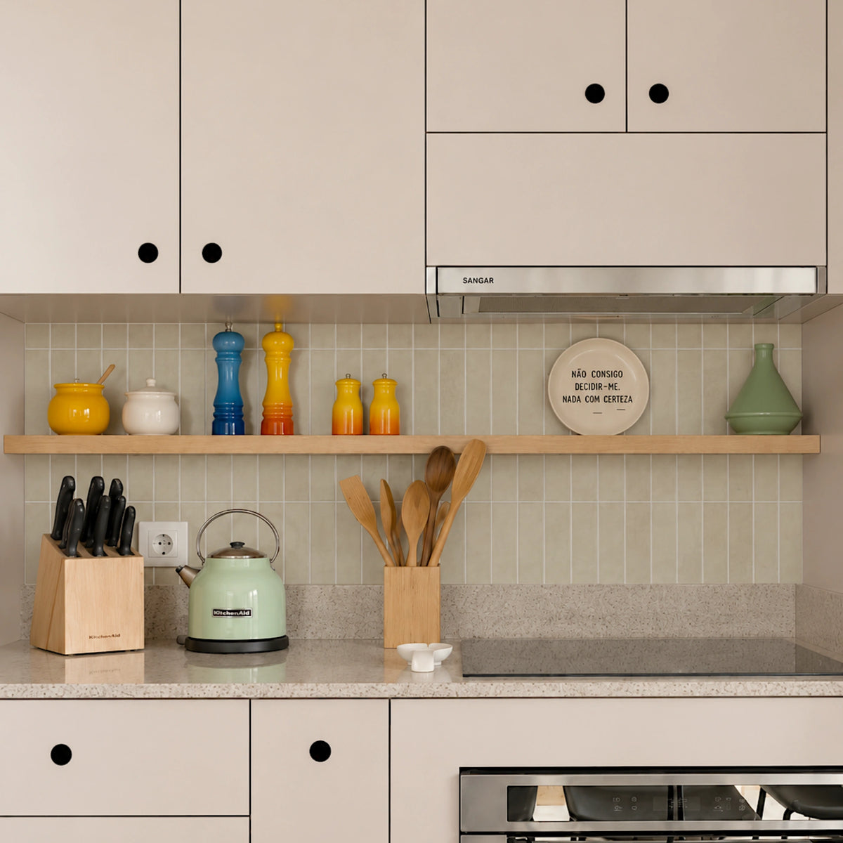 Modern greige kitchen with glossy beige tile backsplash, warm neutral cabinets, wooden shelving, and minimalist kitchen accessories.