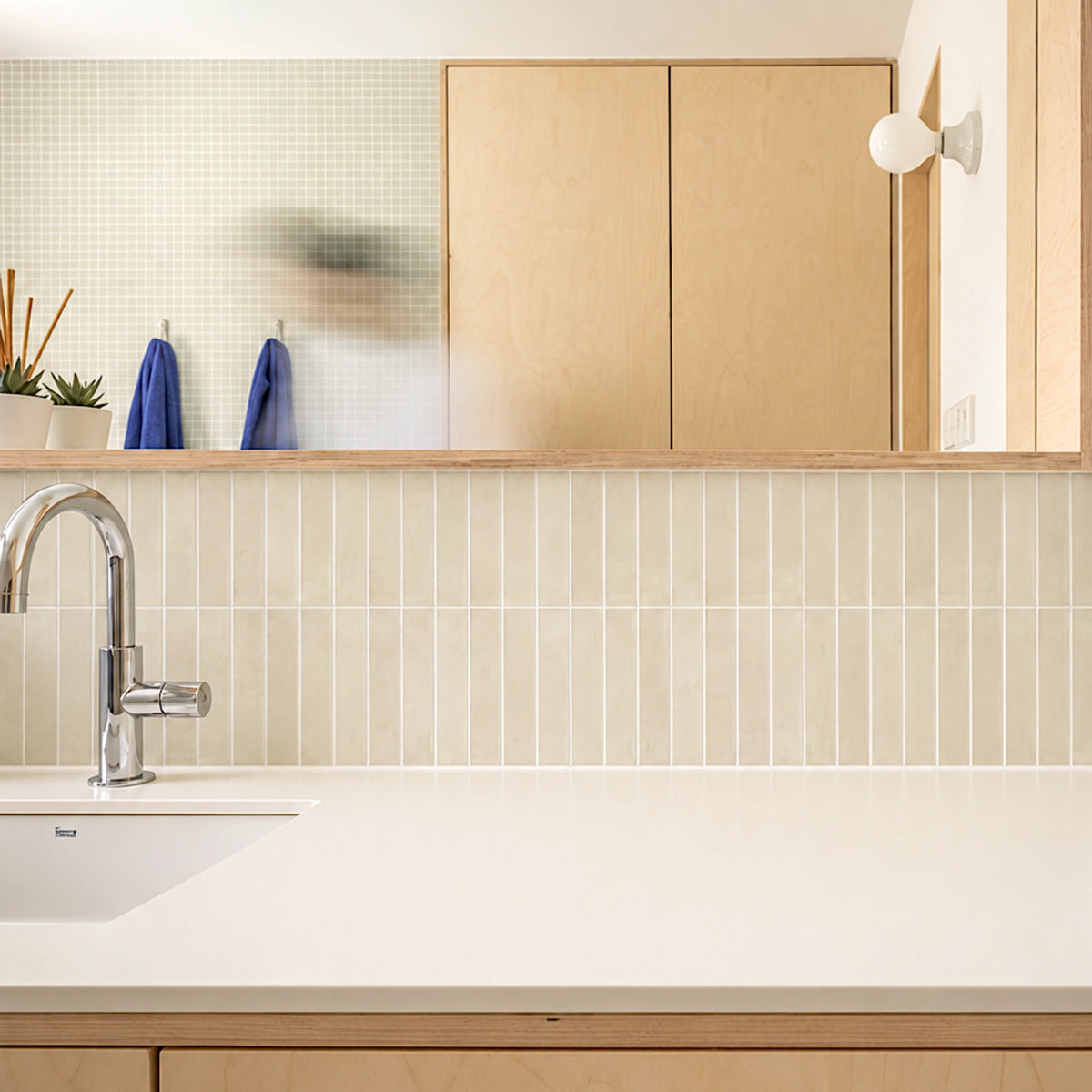 Scandinavian-style kitchen with ivory vertical tile backsplash, light wood cabinets, white countertop, and modern chrome faucet.