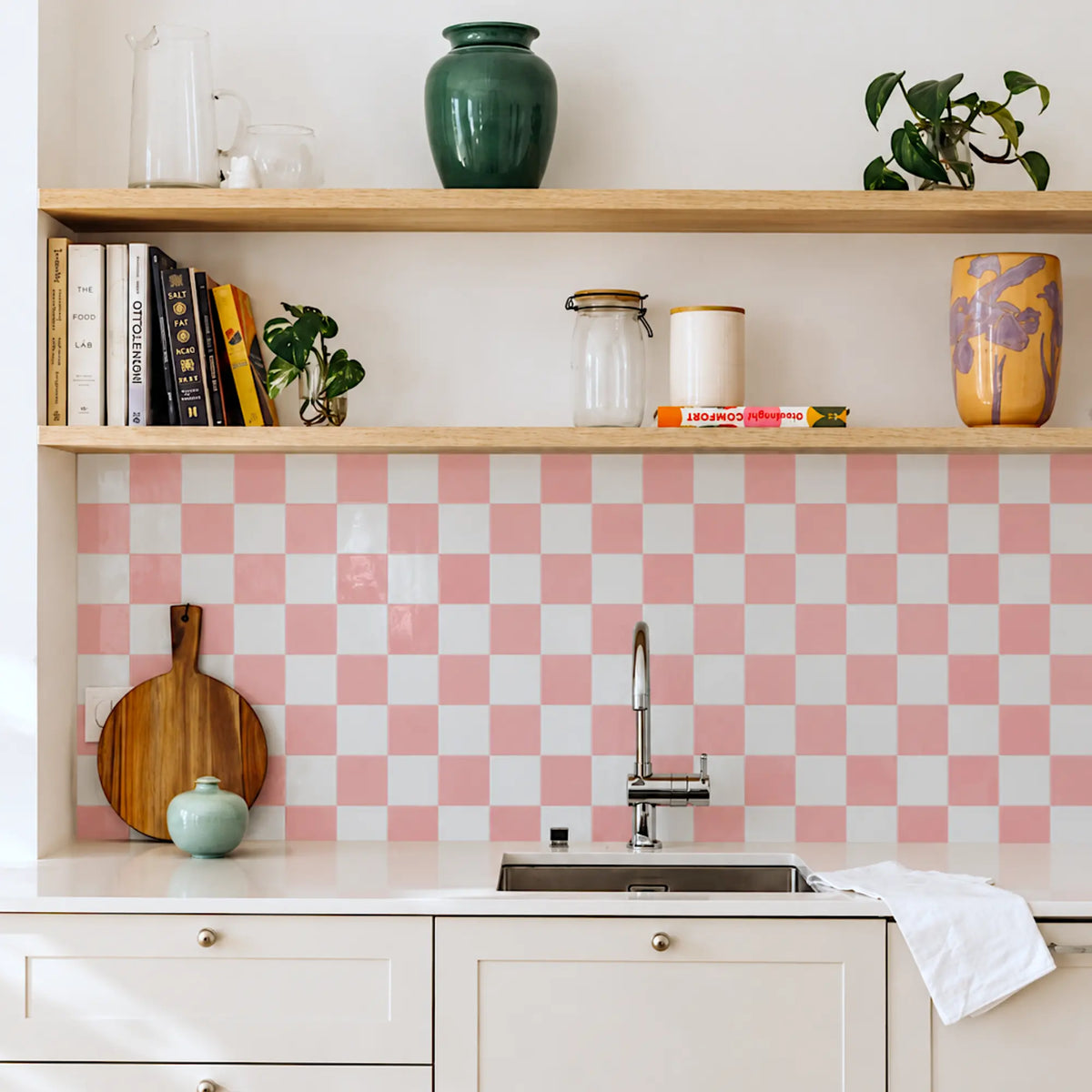 Peach Shore pink and white checkerboard peel and stick backsplash behind a white kitchen sink and wooden shelves