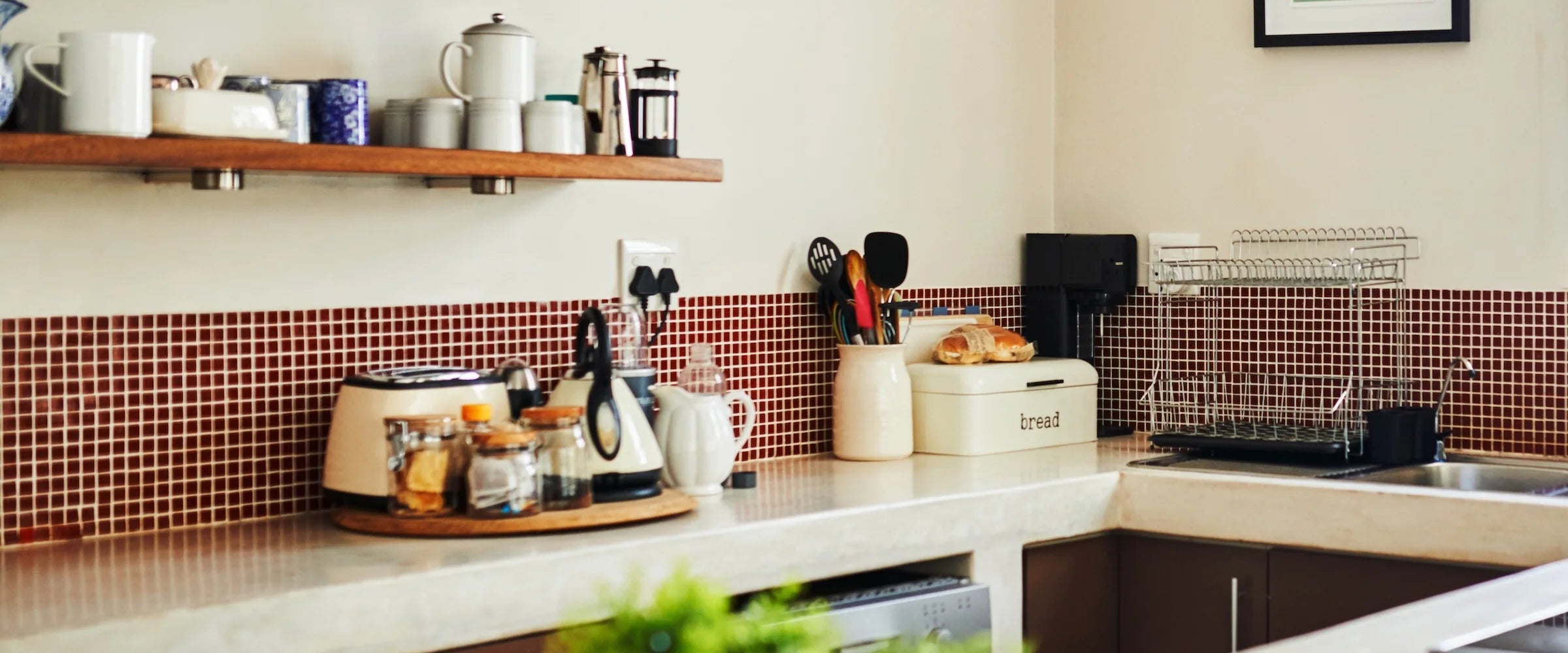 Modern kitchen with Stickwoll peel and stick mosaic tiles in deep red as backsplash; styled with countertop essentials including a bread box, glass jars, a kettle, and a dish rack for a functional and warm aesthetic