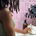 Stickwoll Peel and Stick Moroccan Tiles series in a cozy bathroom setting; featuring pink tiles on the wall, with an African American girl touching a towel on the countertop, styled with a large brown vase for a warm and inviting atmosphere