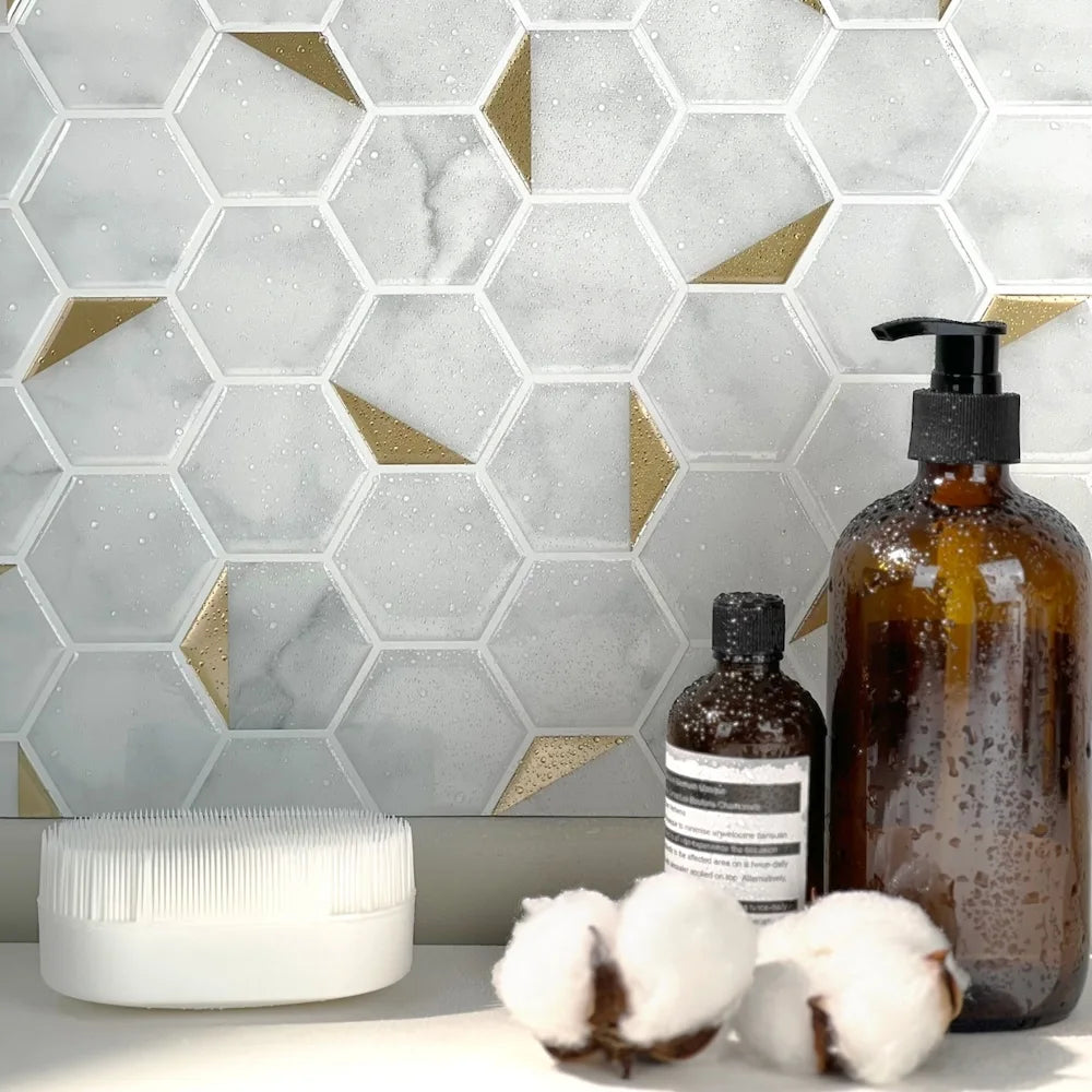 Bathroom scene featuring Stickwoll hexagon tiles with marble and gold accents on the wall, covered in water droplets to highlight the waterproof functionality; styled with amber bottles and cotton for a sleek and elegant look